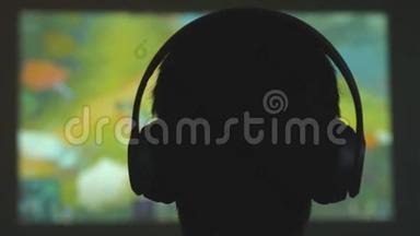 一个年轻人在黑暗的房间里玩电子游戏，用耳机看电影。 3840x2160